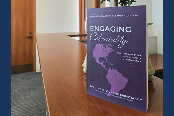 photo of Raimundo Barreto's book "Engaging Coloniality : The Liberative Story of Christianity in Latin America" on a wooden shelf in Wright Library
