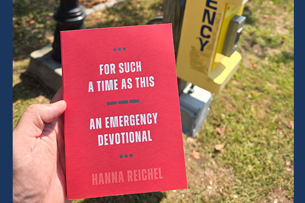 photo of Hanna Reichel's book "For Such a Time as This : an emergency devotional" held in someone's hand outside the library next to an emergency call box